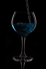 A glass with a blue liquid on a black background