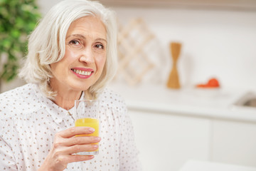 Happy senior woman drinking juice in kitchen