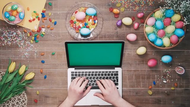 Man using laptop computer with green screen on table decorated with easter eggs Top view