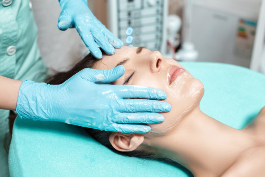 beautician applies face cream on beautiful young woman in Spa salon. cosmetic procedure skin care. 