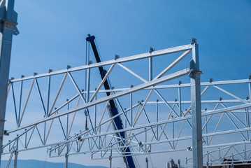 Crane lifting galvanized steel roof truss construction frames with deep blue sky in the background