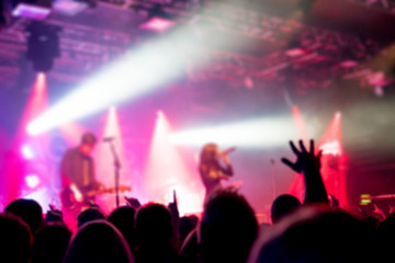 Plakat Blurred background, Bokeh, silhouette of cheering audience, hands up and musicians on the stage with lighting in indoor concert