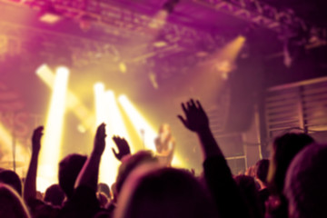 Fototapeta premium Blurred background, Bokeh, silhouette of cheering audience, hands up and musicians on the stage with lighting in indoor concert