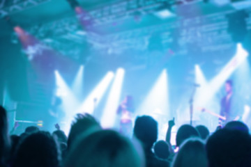 Blurred background, Bokeh, silhouette of cheering audience, hands up and musicians on the stage with lighting in indoor concert