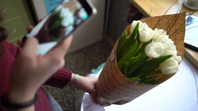 Young woman makes photo of flowers bouqet. Take a photo of gifted tulip