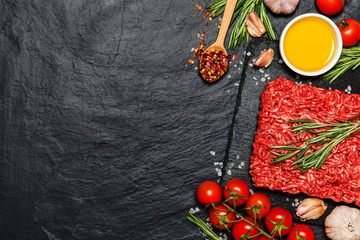 Minced meat on a slate stone black board with seasonings and fresh rosemary on black background, top view - 142518274
