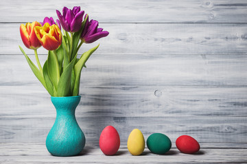 Still life with painted eggs and tulips in vase on wooden background