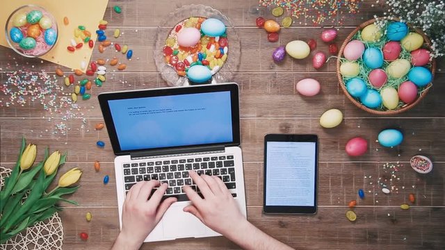 Man using laptop computer and digital tablet on table decorated with easter eggs Top view
