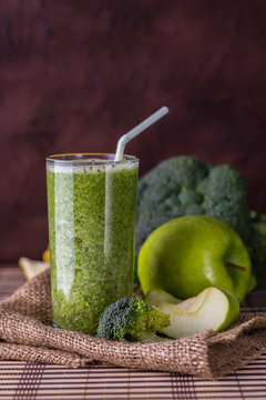 Broccoli smoothie in glass bowl on wooden background with lemon and apple.