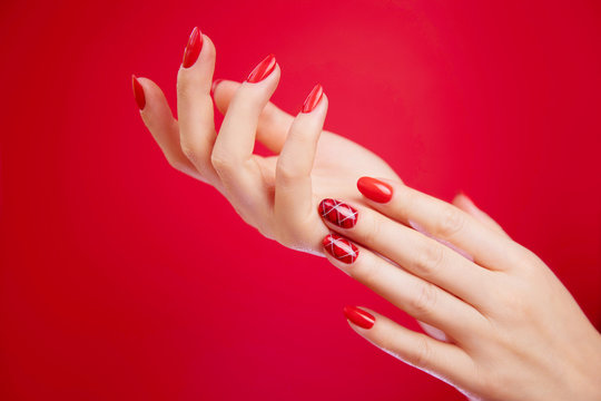  Beautiful manicured woman's hands on red background.