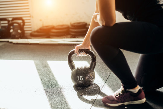 Young fitness woman lifting a heavy weight kettle bell at gym. Caucasian female athlete working out at gym. Fit young lady doing cross fit exercise.
