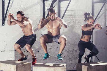 Fit young people doing box jumps as a group in a gym