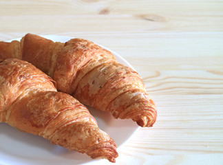 Plate of two fresh butter Croissant pastries served on light color wooden table