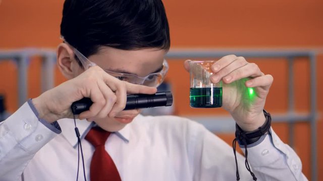Student at school doing a science experiment using reagents, test tube and laser. 4K.