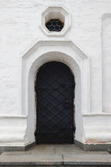 Medieval black door with metal decoration in white wall of orthodox church.