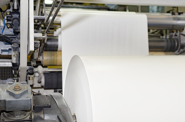 A large webset offset printing press running a long roll off paper over its rollers at high speed