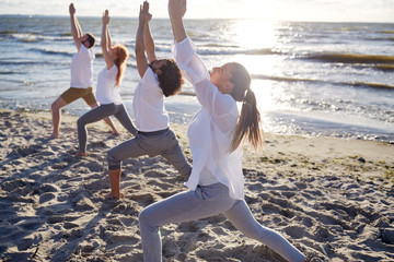 group of people making yoga exercises on beach
