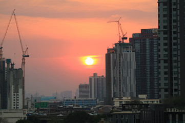 Sun setting on pastel orange sky amongst working cranes of the construction site, Bangkok, Thailand 