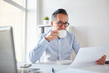 businessman with papers drinking coffee at office