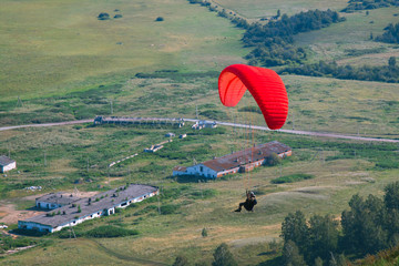 Bright red paraglider flies against the backdrop of an abandoned farm.
