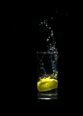 A lemon slice splashes in a glass of water isolated on black background.
