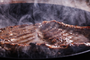 Beef steak fry in a frying pan in smoke and steam
