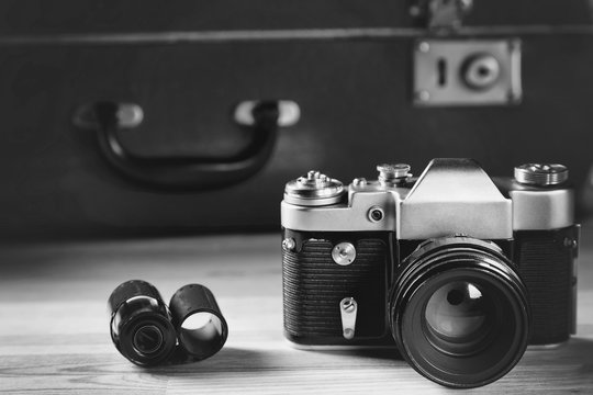 Old film camera with film against the background of a vintage brown suitcase. Black and white image