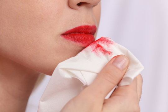 Woman removing make up with cleaning lotion close up. Red lipstick mark on white paper napkin
