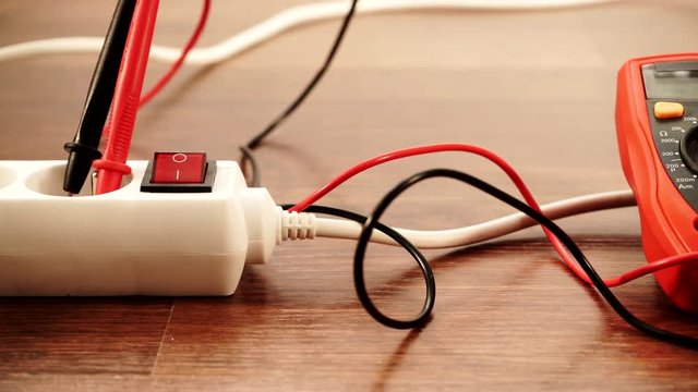 Measurement of voltage in electrical socket extension cord with multimeter on wooden floor background 4K ProRes HQ codec