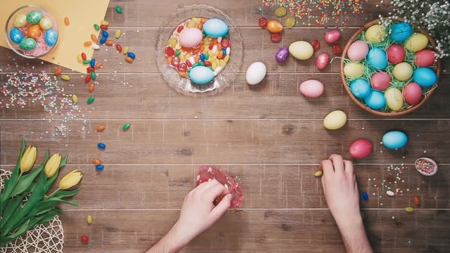 Man putting candys in the bag on table decorated with easter eggs. Top view