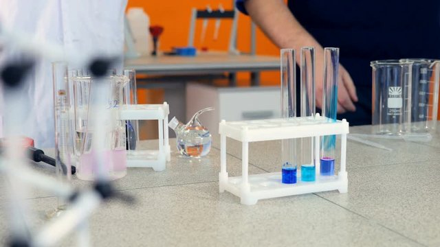 Hand of a lab technician, pharmacist or doctor holding a test tube adding a chemical solution from a pipette during a test or experiment watched by colleagues or students