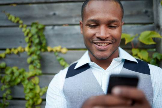 Handsome Black Man Hanging Out And Texting With His Mobile Smartphone Outside Next To A Wooden Fence