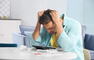 Shocked young man calculating taxes at home