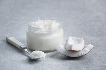 Fresh coconut oil in glassware and spoon on grey background