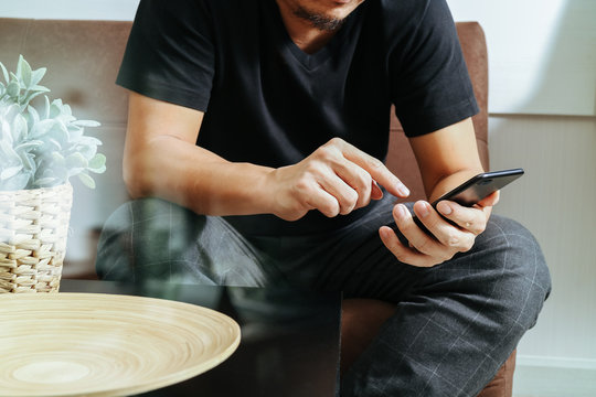 designer man hand using smart phon for mobile payments online shopping,omni channel,sitting on sofa in living room,vase rattan with plant and wooden tray on table,filter