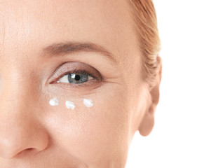Senior woman with facial anti-aging cream on white background