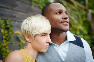 Fototapeta premium Attractive and stylish multicultural couple in love cuddling by a fence in an ivy-filled urban setting