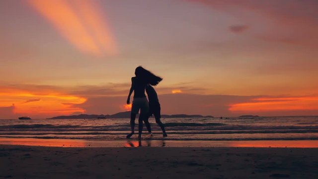 Slow motion silhouette of happy loving couple meet and play at the beach on sunset in ocean shore