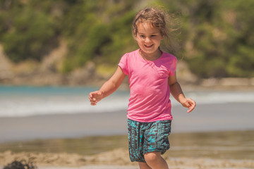 outdoor portrait of young happy smiling child girl playing run on beach