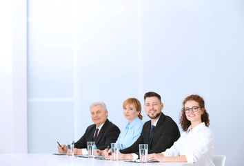 Group of four business people in elegant suits sitting at working desk in light auditorium