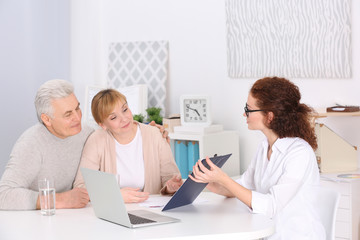 Fototapeta premium Middle aged couple discussing terms of insurance contract with agent sitting at table in office