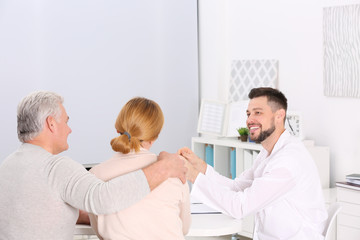 Middle aged couple discussing terms of insurance contract with agent sitting at table in office