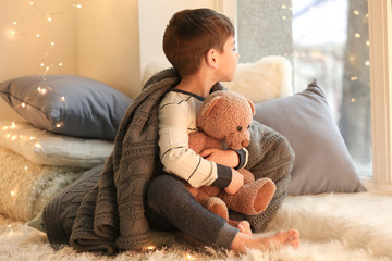 Cute little boy with teddy bear near window at home - Powered by Adobe