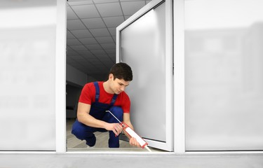 Young worker sealing joints of window in office