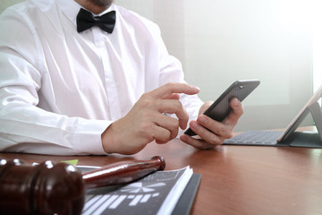 Fototapeta premium Justice and Law context.Male lawyer hand working with smart phone,digital tablet computer docking keyboard with gavel and document on wood table