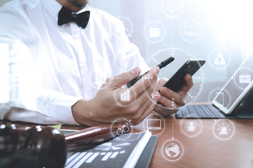 Justice and Law context.Male lawyer hand working with smart phone,digital tablet computer docking keyboard with gavel and document on wood table,virtual interface graphic icons diagram