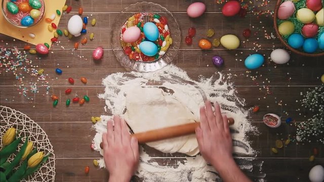 Man kneading dough on table decorated with easter eggs. Top view