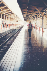 Young hipster man walking in platform looking away while waiting for the train at the railway station. Travel concept.