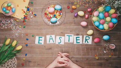 Man puts word Easter on table decorated with easter eggs. Top view
