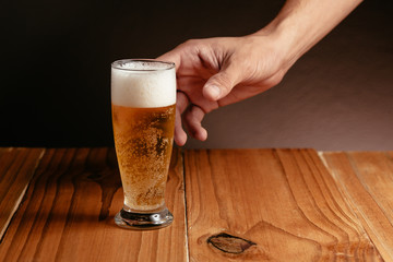 Close up of a male hand taking a glass of beer from wood table